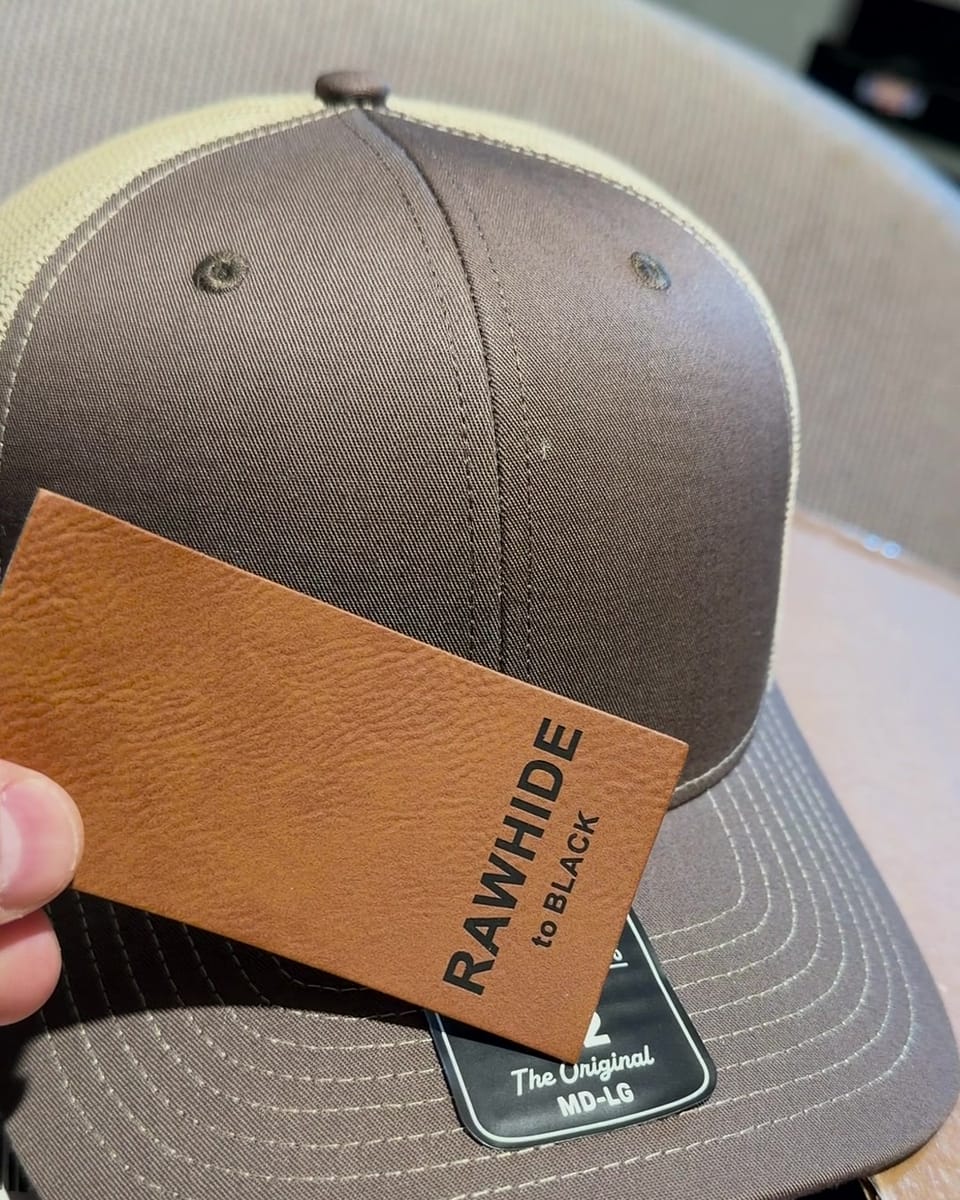 A piece of Rawhide leatherette, labeled Rawhide to black, held against a Brown/Khaki hat